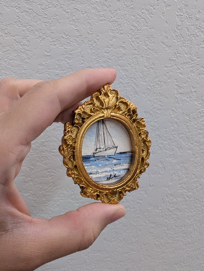 a hand holding a miniature picture of a sailboat