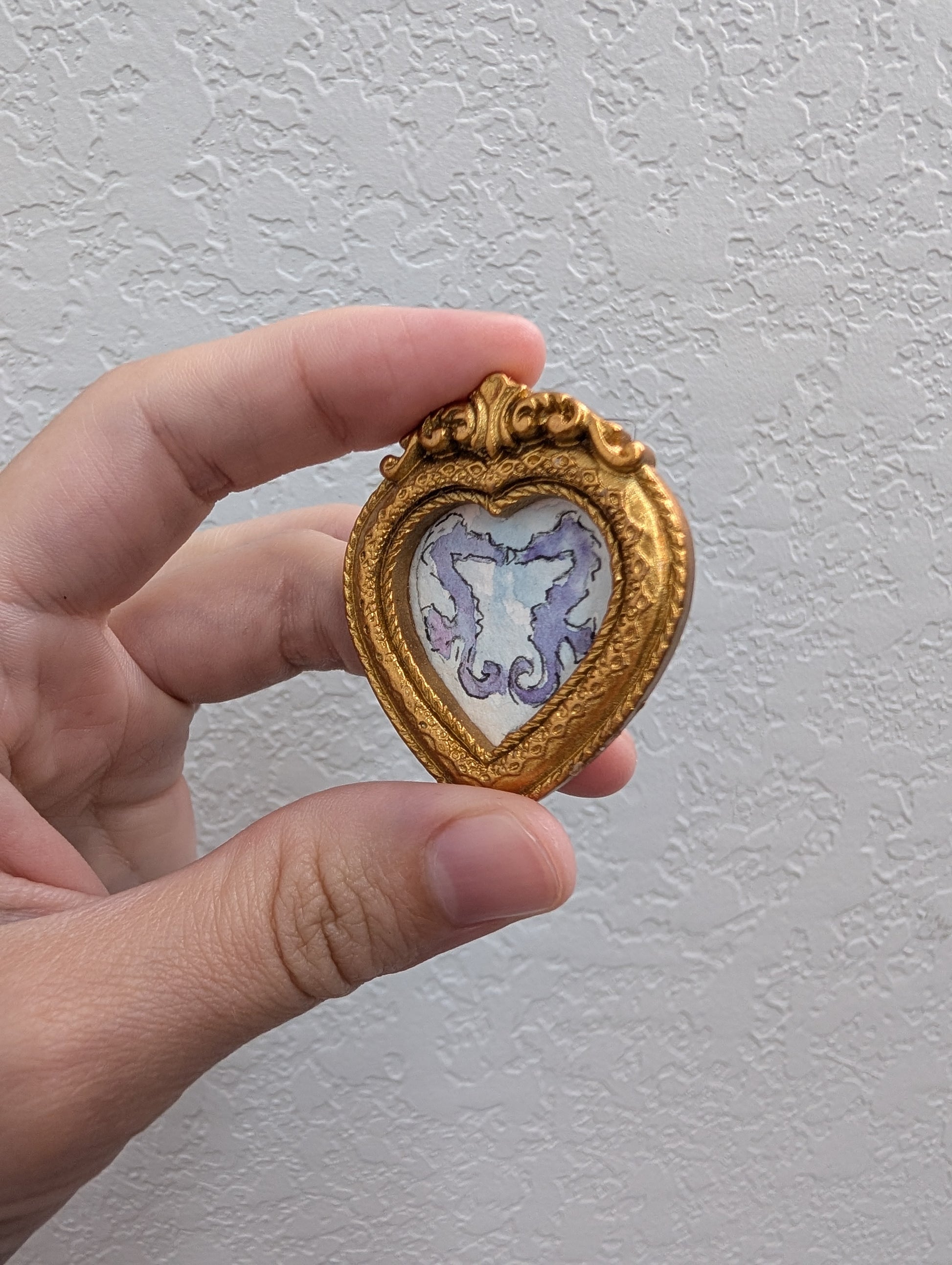 a hand holding a small heart shaped brooch
