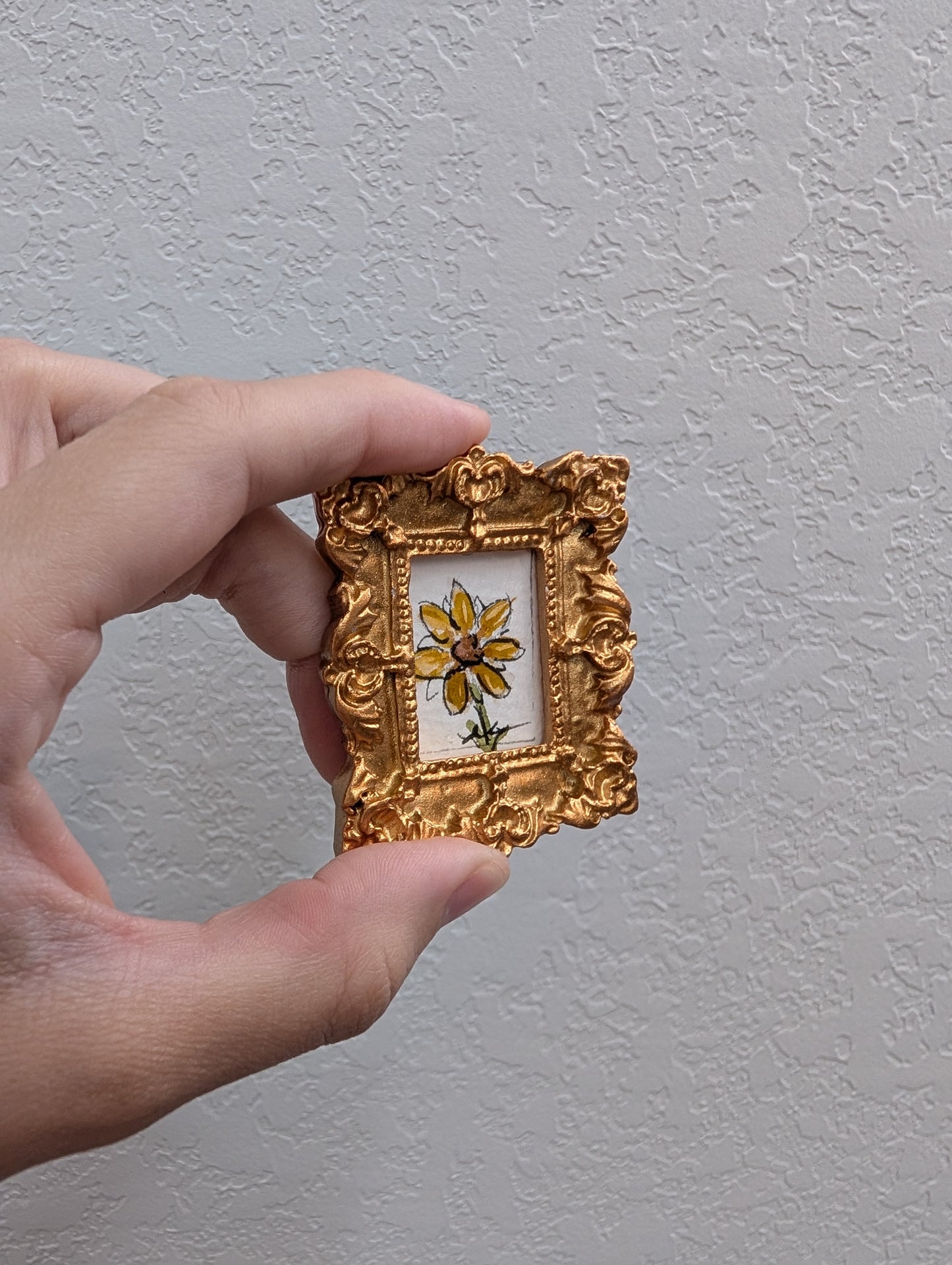 a person holding a small picture frame with a flower painted on it