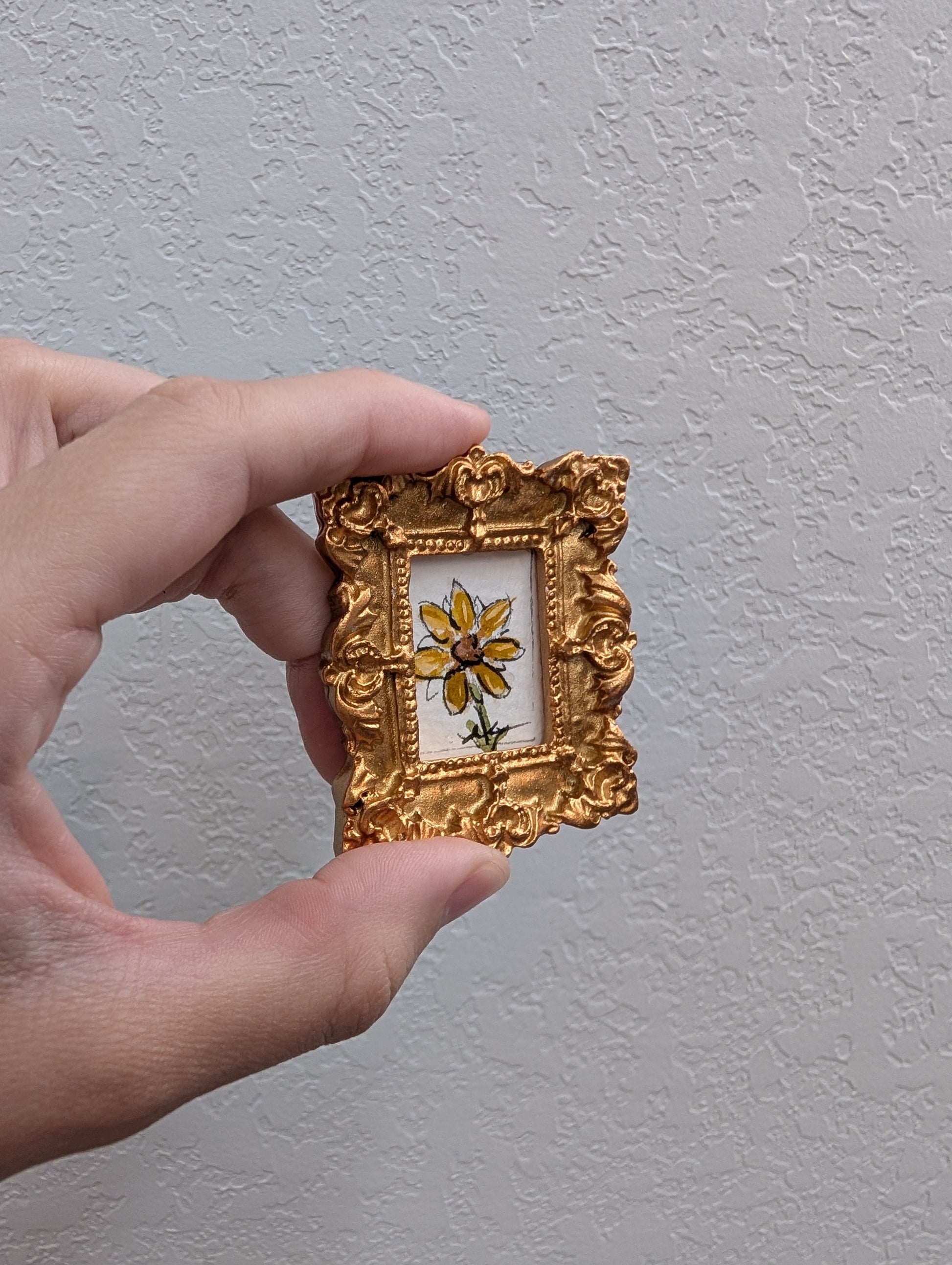 a person holding a small picture frame with a flower painted on it